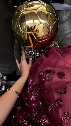 a person holding a golden soccer ball on top of a black leather chair with pink and gold sequins