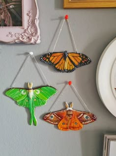 three colorful butterflies hanging from chains on a wall next to a clock and framed pictures