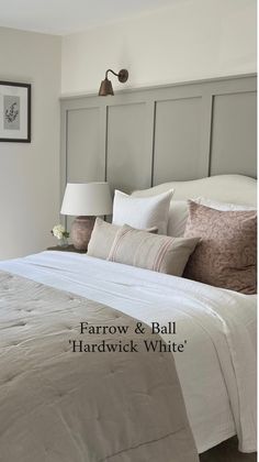 a bed with white sheets and pillows next to a wall mounted headboard in a bedroom