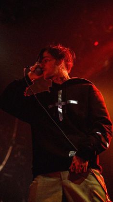 a man standing on top of a stage holding a microphone to his ear and wearing a black hoodie