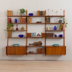 a wooden shelf with books and vases on it in front of a white wall