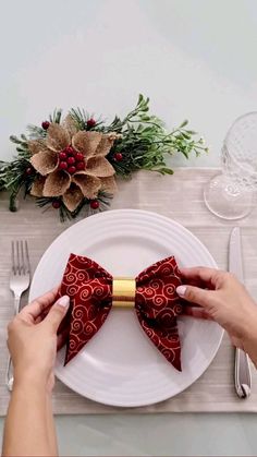 two hands are holding a red bow tie on a white plate