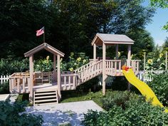 a wooden play set in the middle of some bushes and trees with a yellow slide