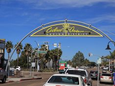 cars are driving under an arch on the street in front of buildings and palm trees