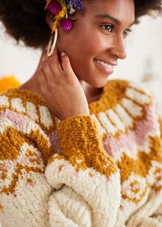 a woman with flowers in her hair smiles at the camera while wearing a colorful sweater