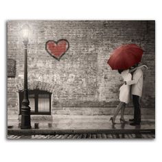 a couple kissing under an umbrella in front of a brick wall with a heart painted on it