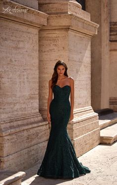 a beautiful woman in a green dress standing by some stone pillars and columns with her hands on her hips