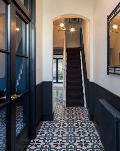 a hallway with black and white tile flooring next to a stair case in a home