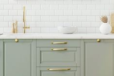 a kitchen with green cabinets and white tile backsplash, gold handles and brass pulls