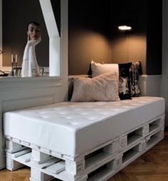 a white bed sitting on top of a hard wood floor next to a wall mounted mirror