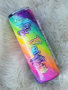 a rainbow colored tumbler with the words happy new year on it sitting on a fluffy white surface