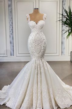 a wedding dress on display in front of a white wall with a potted plant