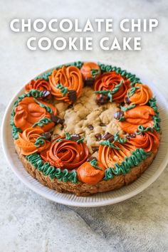 a chocolate chip cookie cake decorated with orange and green icing on a white plate