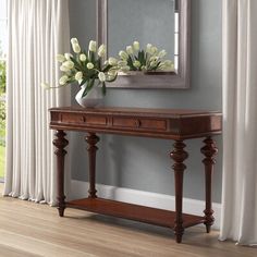 a vase with flowers sitting on top of a wooden table next to a mirror and window