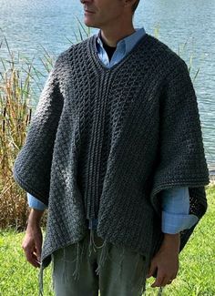 a man standing in front of a body of water wearing a knitted shawl