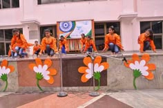 some people are sitting on the side of a wall with orange shirts and flowers painted on them