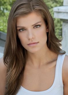 a beautiful young woman with long brown hair posing for a photo in white tank top