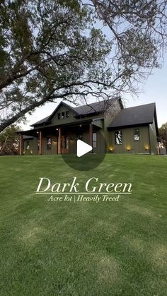 the dark green house is located in front of a large tree and grass field with trees