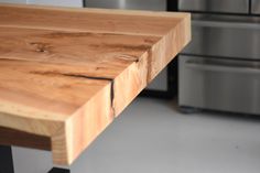 a close up of a wooden table in a room with stainless steel appliances behind it