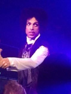 a man in a vest and tie standing on stage with his arm extended out to the side