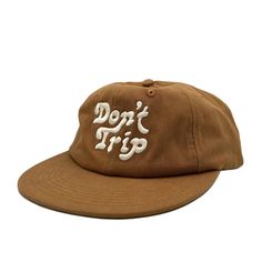 On a white background is a brown unstructured 6 panel baseball hat with white embroidery that reads, Don't Trip. Vintage Beach Baseball Cap With Flat Bill, Vintage Flat Bill Baseball Cap For Beach, Summer Travel Snapback Hat With Flat Bill, Trendy Cotton Baseball Cap For Vacation, Everyday Brown Snapback Hat With Flat Bill, Brown Flat Bill Cotton Hats, Everyday Summer Trucker Hat With Flat Bill, Brown Cotton Trucker Hat With Flat Brim, Vintage Snapback Baseball Cap For Beach