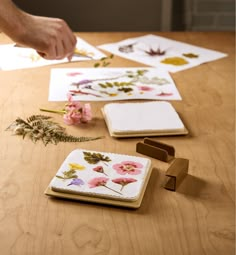 a person is cutting paper with scissors on a wooden table next to flowers and leaves