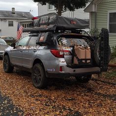 the back end of a silver suv with luggage on it parked in front of a house