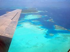 an airplane wing flying over the ocean and coral reefes in the water below it