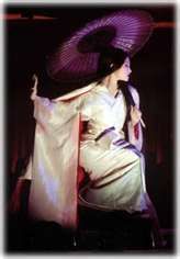 a woman with an umbrella sitting on a stool in front of a stage curtain and wearing a kimono