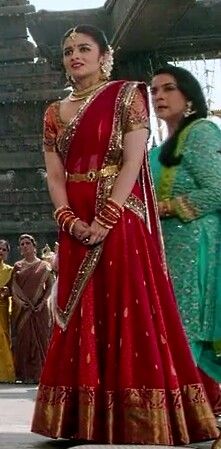 a woman in a red and gold bridal gown standing next to other women wearing green sari