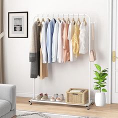 a rack with clothes hanging on it next to a couch in a white living room