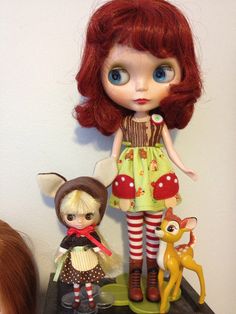 a doll with red hair standing next to two other dolls on a shelf in front of a white wall