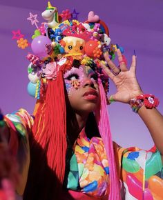 a woman with colorful hair and decorations on her head is holding her hands up to her face