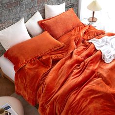 an orange comforter and pillows on a bed with brick wall in the back ground