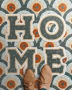 someone's feet standing in front of a mosaic floor with the word home on it