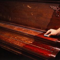 a man is using a mouse to clean an old, wooden piano with red stain