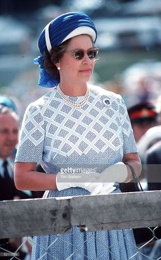 the queen of england is wearing a blue dress and white gloves while standing behind a fence