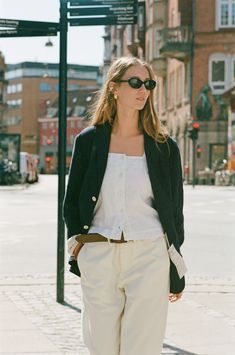 a woman walking down the street wearing white pants and a black blazer with sunglasses on