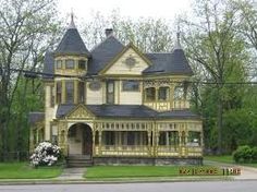 an old victorian style house in the middle of a street with trees and bushes around it