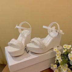 a pair of white high heeled shoes sitting on top of a box next to flowers