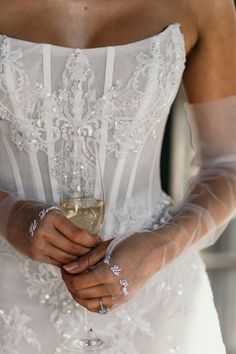 a woman in a wedding dress holding a glass of wine and wearing gloves on her arm