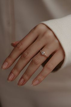 a woman's hand with a diamond ring on her left hand, wearing a white sweater