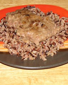 an orange plate topped with rice covered in gravy on top of a wooden table