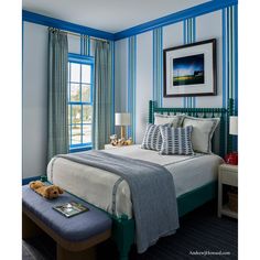 a bedroom with blue and white striped walls, a bed in the corner and a teddy bear on the foot board