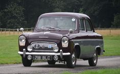 an old car driving down a road in the country side with trees in the background