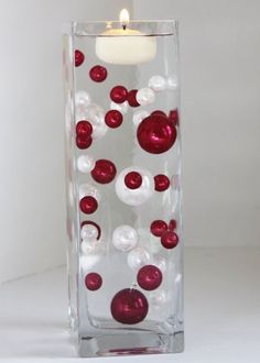 a tall glass vase with red and white balls in it, lit by a candle