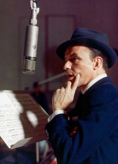 a man in a suit and hat holding a sheet while standing next to a microphone