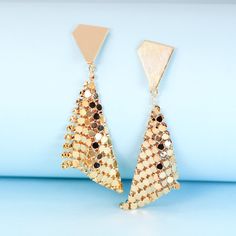 These geometric gold plated earrings will add instant sparkle and shine to any outfit. The handkerchief-inspired dangle design creates movement when you walk, catching the light in a unique way. The triangle stud backs ensure they'll stay put all night long, through dancing, laughing and all the festivities. Perfect party earrings for fashion-forward gals seeking a statement accessory that stands out from the crowd. Materials: 24k gold plated brassDimensions: 2.61 x 0.92 in Jewelry Care: See more information about how to care for your jewelry here. Shipping Policy: Orders will be shipped within 1-3 business days. Economy shipping will take 7-14 days to arrive and standard shipping is 1- 4 days for U.S. orders. International shipping time is depended on the country and per shipping method. Diamond-shaped Gold Jewelry For Party, Gold Diamond-shaped Party Jewelry, Gold Geometric Jewelry For Party, Trendy Gold Chandelier Earrings For Evening, Trendy Gold Triangle Earrings, Triangle Gold Metal Earrings, Gold Triangle Metal Earrings, Gold Geometric Earrings For Party, Geometric Gold Earrings For Party