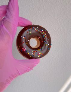 a person in pink gloves holding up a chocolate doughnut with sprinkles