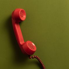 an old fashioned red telephone on a green background with the cord still attached to it